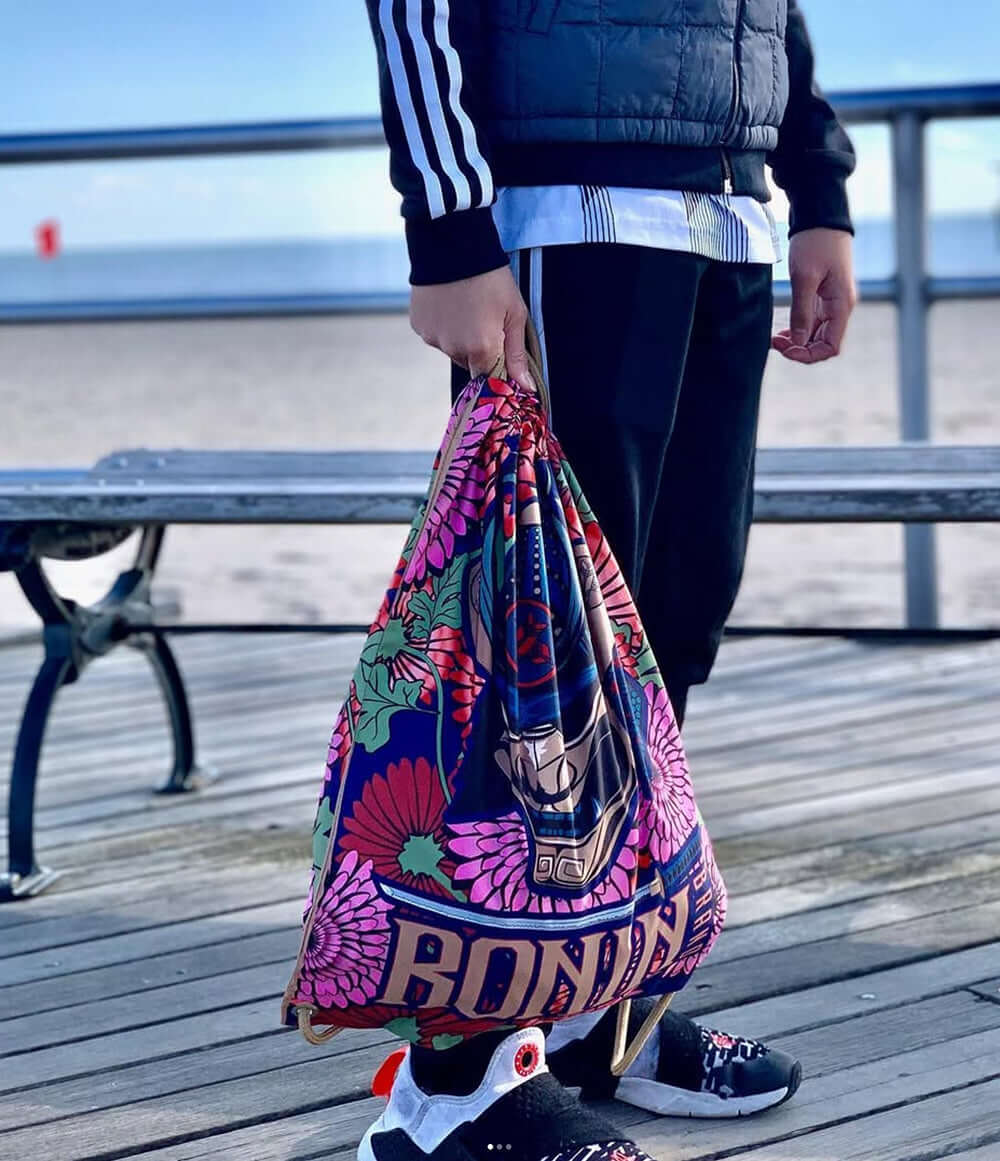 Person holding a colorful Ronin bag on a boardwalk, highlighting BJJ and Boxing styles from Paragon x Superare x Ronin.