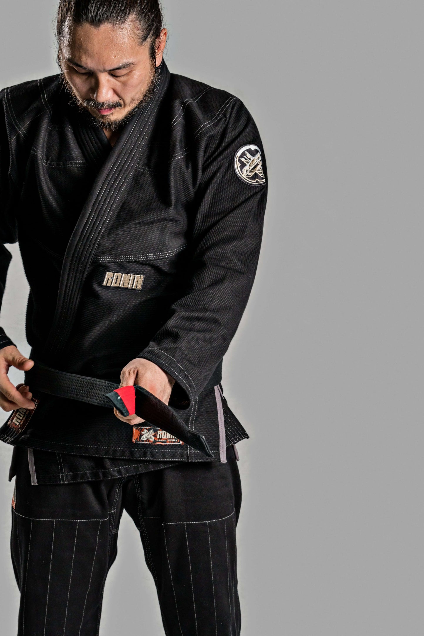 Man adjusting his Roninbrand Kurosawa BJJ Gi in black, showcasing comfort and fit for Brazilian Jiu Jitsu.