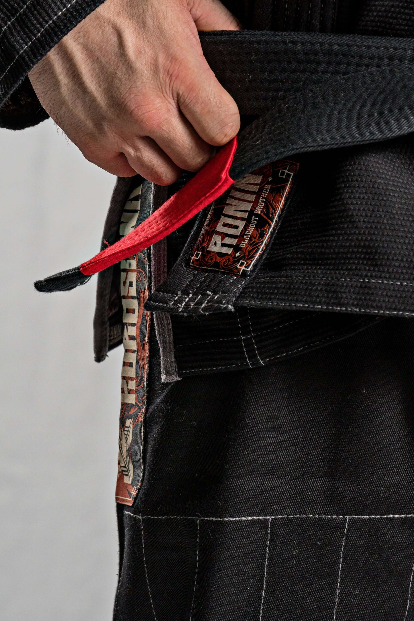 Hand adjusting the red belt of the Roninbrand Kurosawa BJJ Gi, showcasing premium fabric and design for Brazilian Jiu Jitsu.