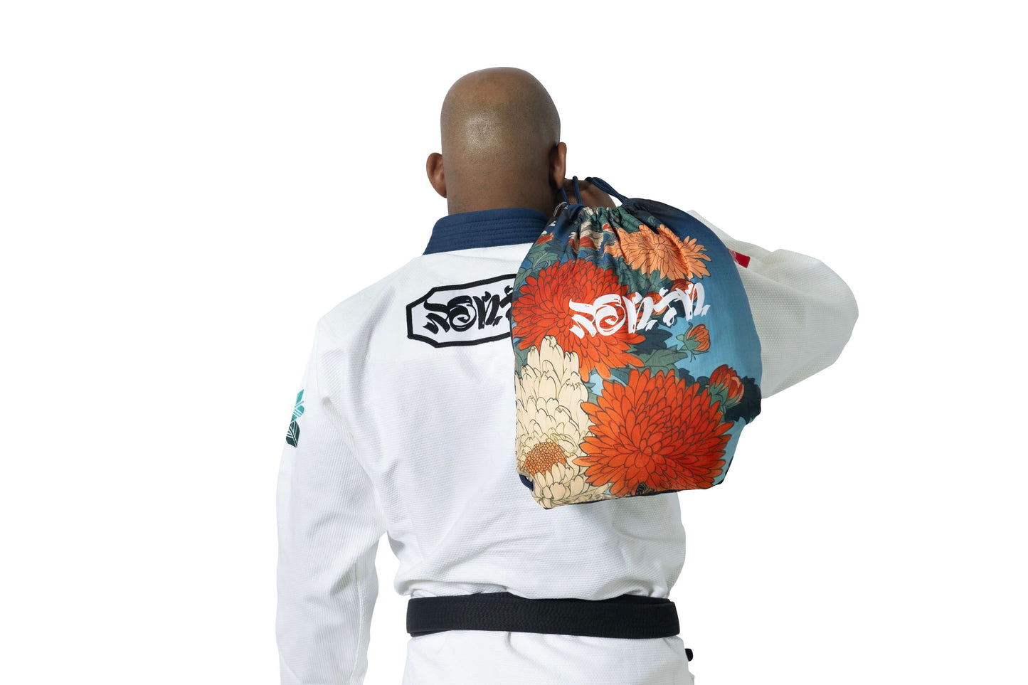 Man in white BJJ gi with Ronin logo, carrying a floral training bag, symbolizing strength and style in Brazilian Jiu Jitsu.