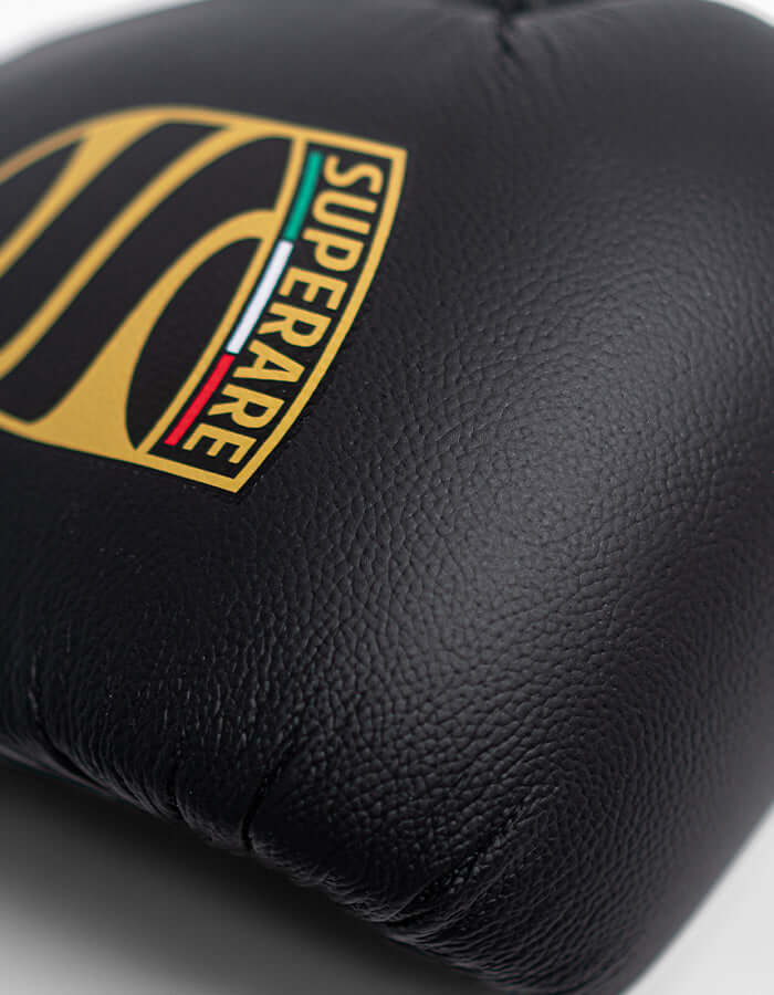 Close-up of Superare S50 boxing gloves logo, showcasing sleek matte black leather design and craftsmanship.