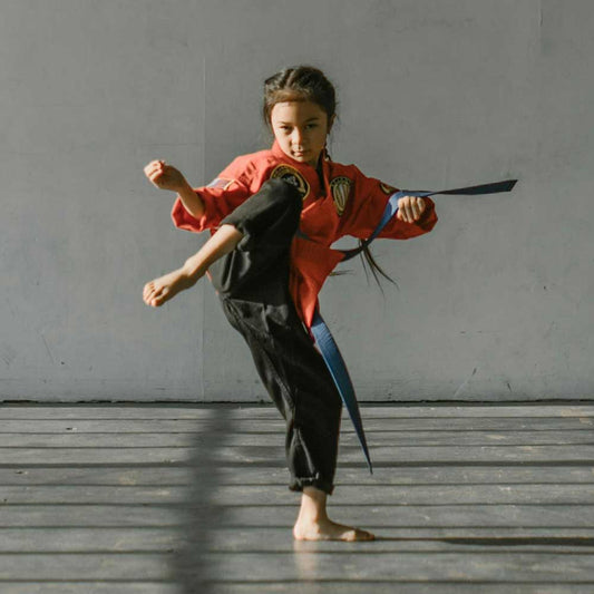 Child performing a martial arts kick in a red uniform, showcasing agility and focus in a training setting.