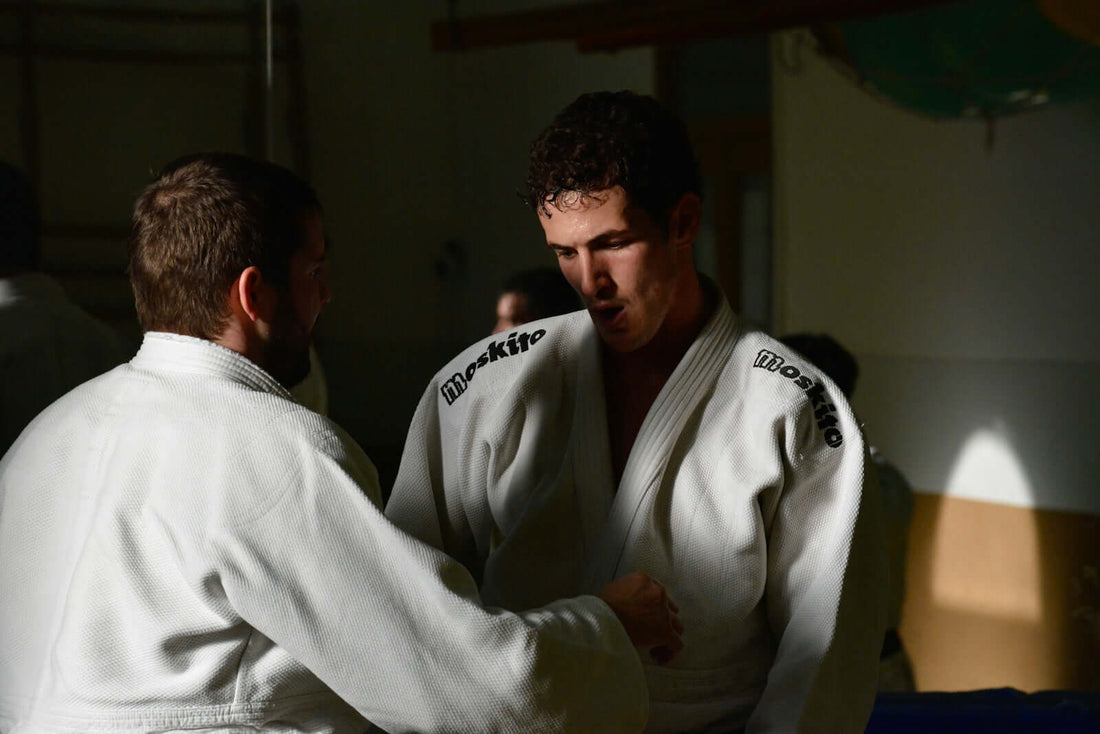 Fight: Two practitioners in professional BJJ gis training in a dojo, demonstrating techniques and martial arts skills.