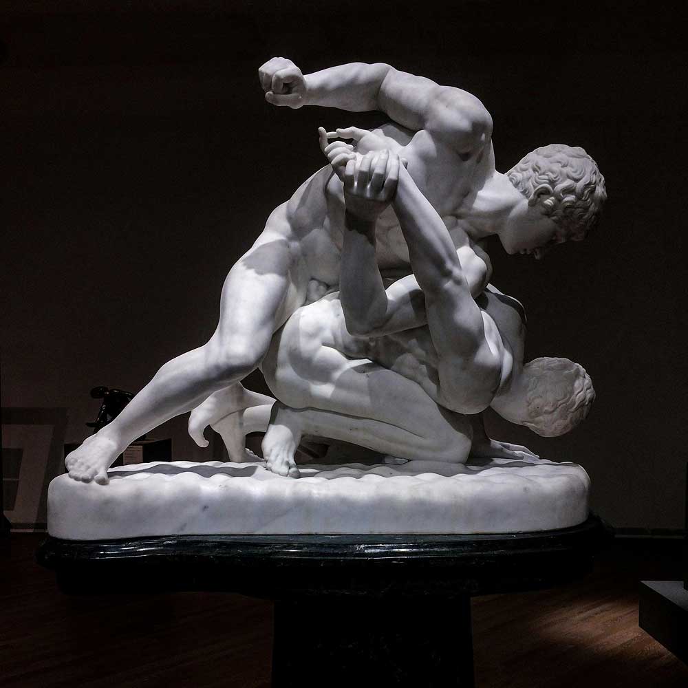 White marble sculpture of two wrestlers engaged in combat, highlighting strength and athleticism.
