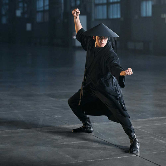 Martial artist performing a traditional pose, showcasing skills and resilience in a dramatic setting.