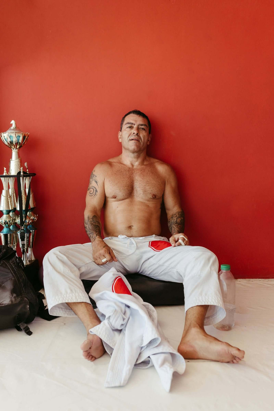 Fight scene with a martial artist resting on the floor in a training space, wearing Brazilian jiu-jitsu gear.