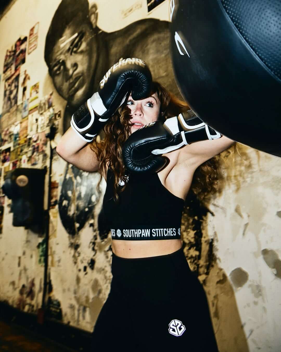 A female boxer in gloves practicing in front of a mural, showcasing the dedication to the sport of Boxing.Paragon Elite Fight