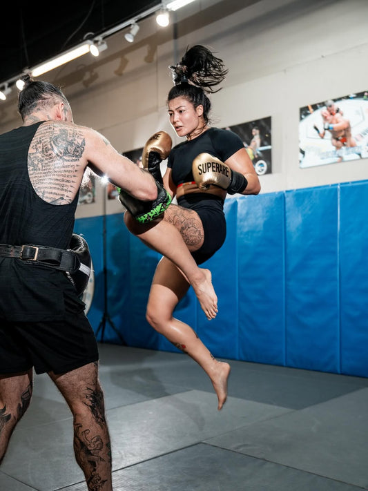 Boxing training session showcasing a female fighter practicing with heavy bag gloves in a gym.