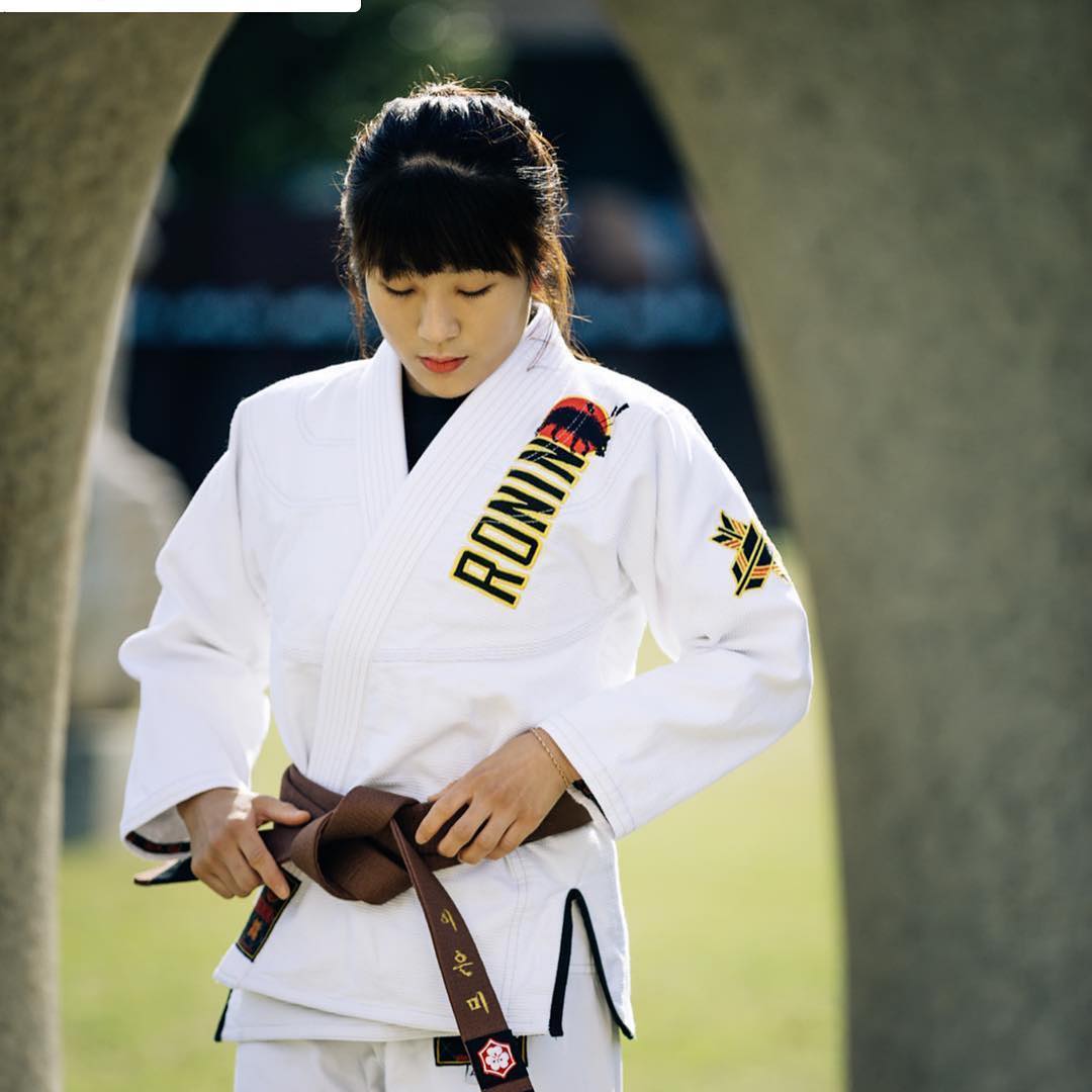 A practitioner adjusting her brown belt in a Jiu Jitsu gi, demonstrating proper fit for training.