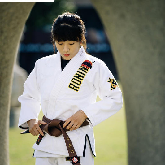 A practitioner adjusting her brown belt in a Jiu Jitsu gi, demonstrating proper fit for training.