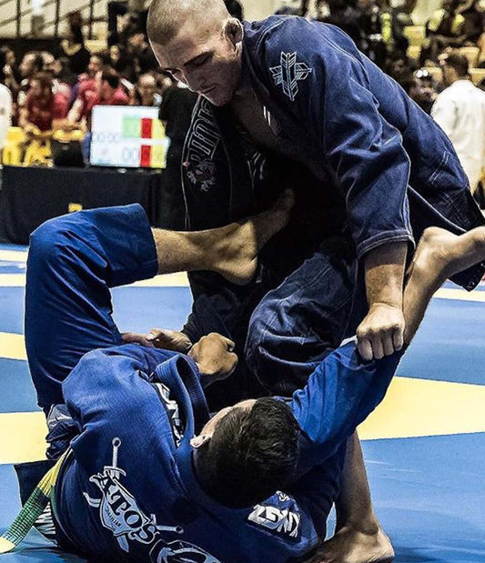 Two Brazilian Jiu Jitsu athletes competing in an intense match on the mat during a tournament.