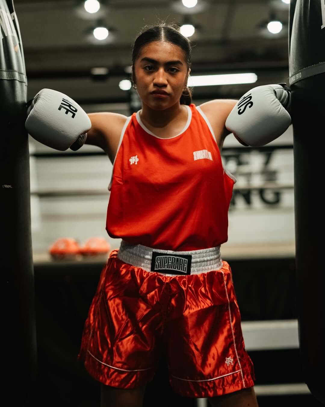 Female boxer in red gear posing in a gym, emphasizing Boxing training and preparation.