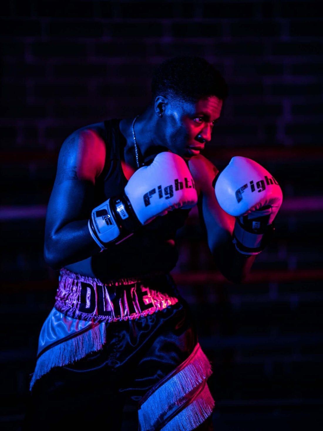 Boxing athlete wearing shimmering gloves in a striking blue and pink setting, focused on sparring practice.