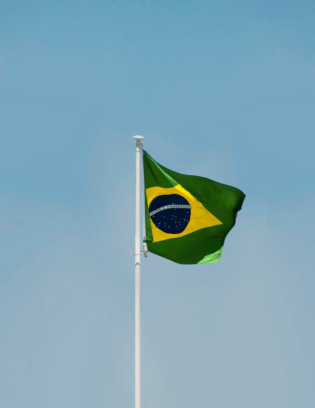 Brazilian flag waving against a clear blue sky, showcasing the colors of Brazil in relation to BJJ culture.