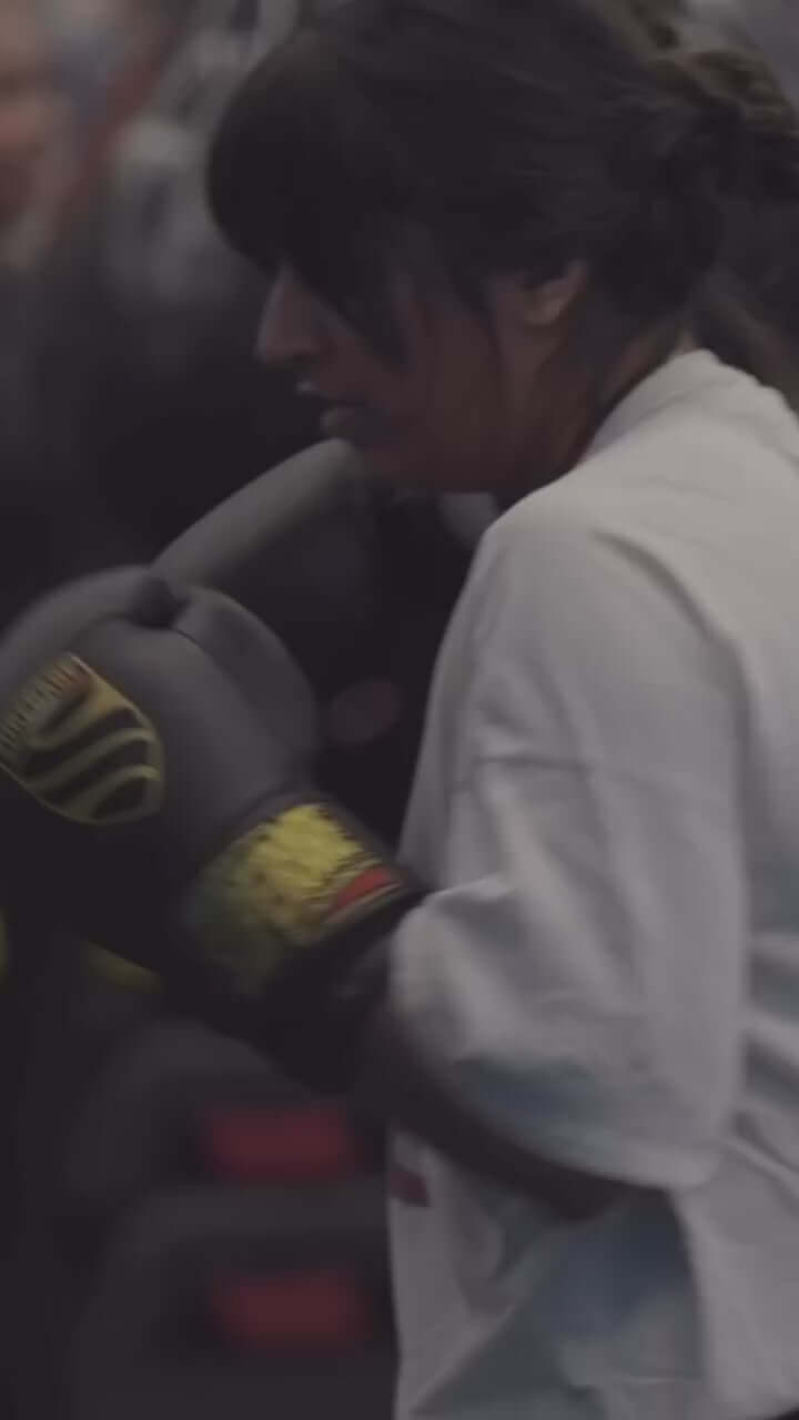 Woman training with boxing gloves in a gym, showcasing dedication and strength in her workout.