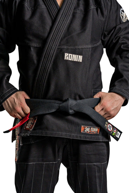 Roninbrand Kurosawa BJJ Gi in black with a fighter tightening their belt, symbolizing honor and legacy in Brazilian Jiu Jitsu.